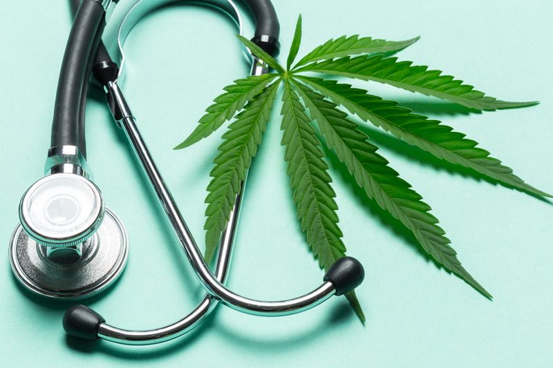 A cannabis leaf next to a stethoscope on a turquoise background