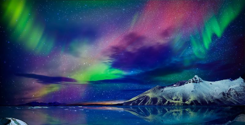 brightly coloured aurora in the night sky over a lake and snow-capped mountains