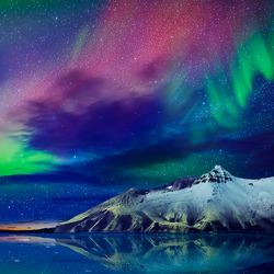 brightly coloured aurora in the night sky over a lake and snow-capped mountains