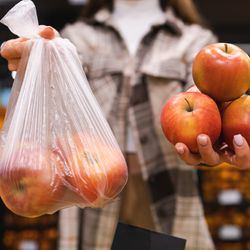 Woman is thinking whether to take apples in a plastic bag or do without. Girl buys fruit in a supermarket. Concept of a world without plastic