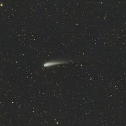 The comet is at the center of the image among a starry background. A wispy tail is easily seen extending from it into space