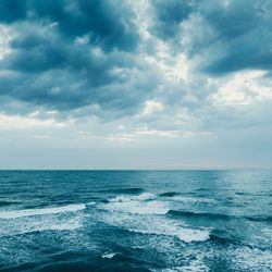 Waves across a dark blue sea with dark clouds fractures by light above