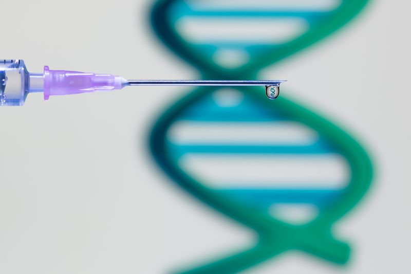 syringe needle with droplet of vaccine containing tiny DNA molecule, with large green DNA molecule out of focus in the background