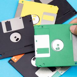 A hand holding one floppy disk with five more on th etable underneath