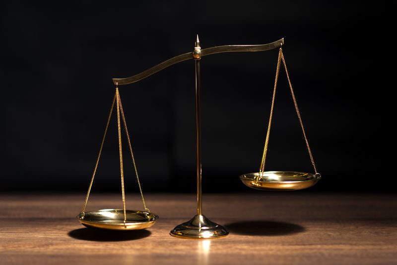 Golden scales on a wooden table on a black background, left hand dipping down