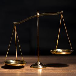 Golden scales on a wooden table on a black background, left hand dipping down