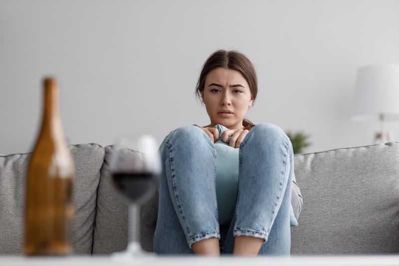 young woman staring anxiously at a bottle and glass of wine