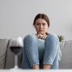 young woman staring anxiously at a bottle and glass of wine