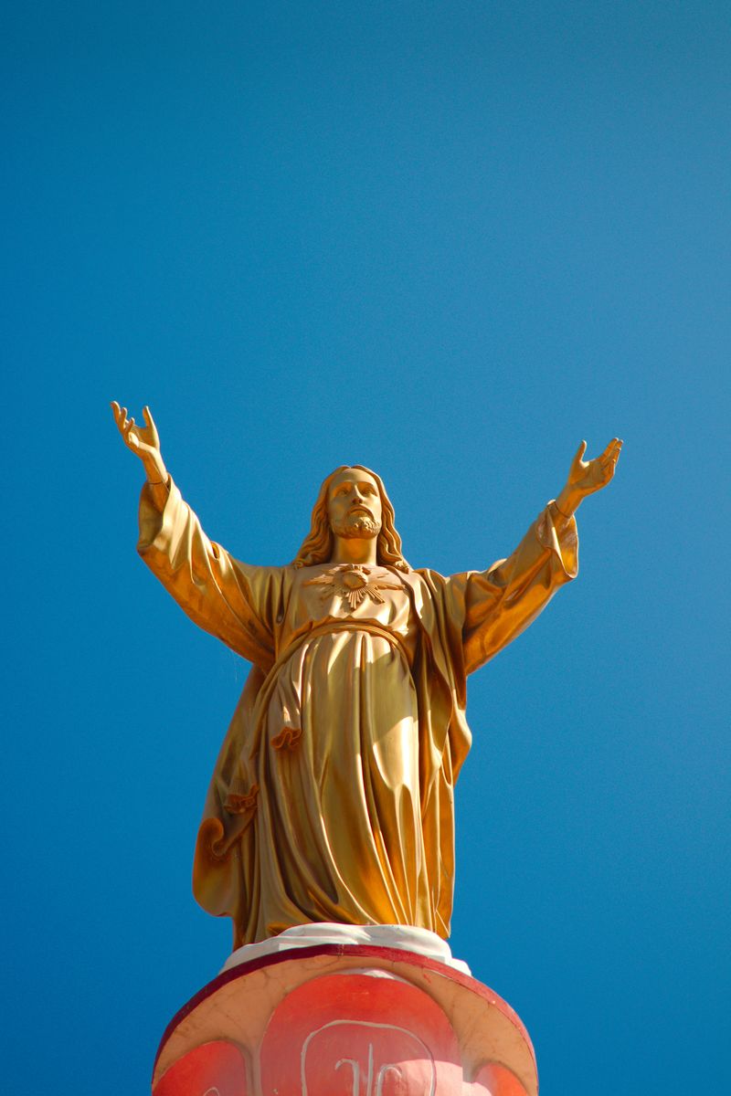 A gold statue of Jesus Christ opening his arms against a blue sky