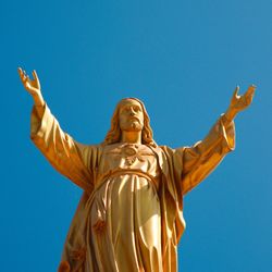 A gold statue of Jesus Christ opening his arms against a blue sky