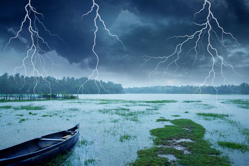 Flashes of lightning in a storm hitting a deserted lake with a wooden boat in