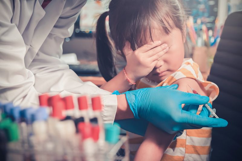 little girl covers her eyes while doctor injects her with a vaccine