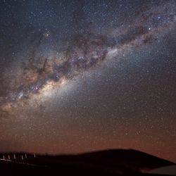 This photograph shows an edge-on view of the Milky Way’s glowing plane slicing across the night sky, laced by bands of dust and dark gas. Taken with a digital camera using a three-minute exposure, the photograph also reveals a bit of action on the ground. To the left, a vehicle with its parking lights on stops lets out a passenger. Though bathed by the light of the Milky Way, the high-altitude desert remains quite dark. To illuminate the rightward path to the underground entrance ramp of the ‘Residencia’, where staff and visitors stay, the passenger takes along a small flashlight, seen as a squiggly bright line. In the lower right, the glass dome on the Residencia’s roof reflects the starry sky overhead. One of our Milky Way’s galactic satellites, the Large Magellanic Cloud, is seen hanging above the Residencia in the lower right corner of the image.