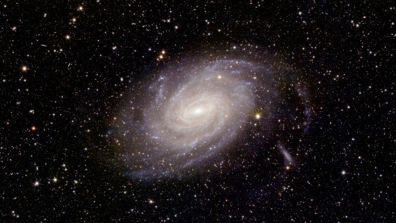 A beautiful spiral galaxy is seen at the center of the image. The sky behind it is full of more distant galaxies