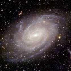 A beautiful spiral galaxy is seen at the center of the image. The sky behind it is full of more distant galaxies