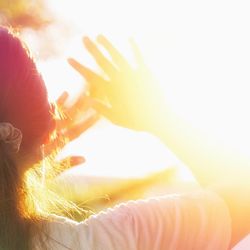 Person with dark hair in a ponytail holding their hands up to shield themselves from the bright sun