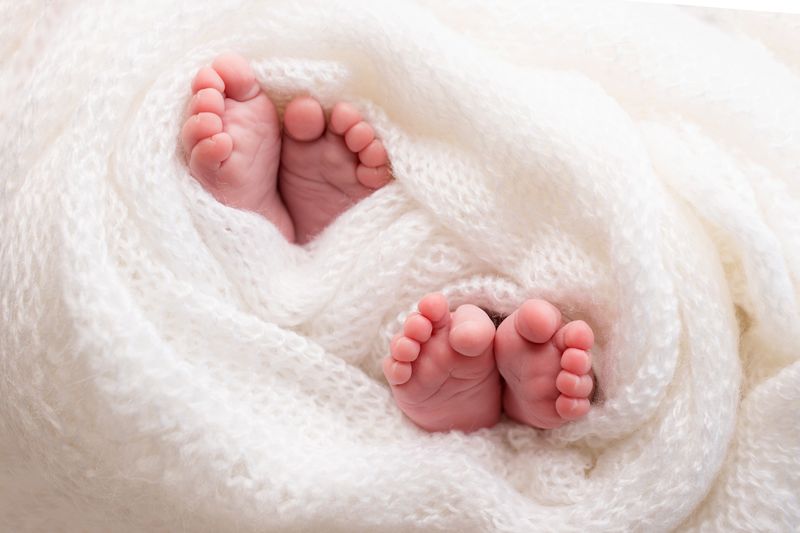 Photograph of two pairs of baby feet wrapped up in a white blanket