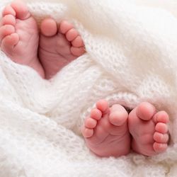 Photograph of two pairs of baby feet wrapped up in a white blanket