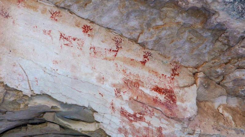 Looking up from Bright Angel Trail, a row of red pictograph deer are visible under an overhang.