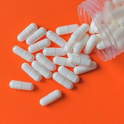 unlabelled bottle of blank, white capsules spilling out onto an orange surface