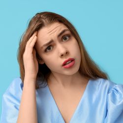 Thoughtful young woman trying to remember something on blue background.