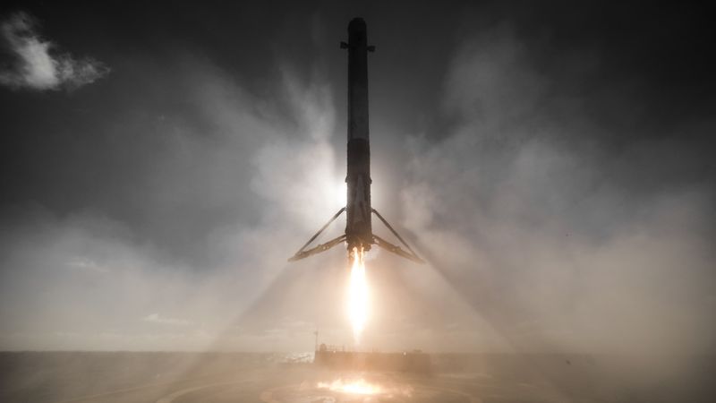 a rocket booster firing a retrorocket as it is about to land on a barge