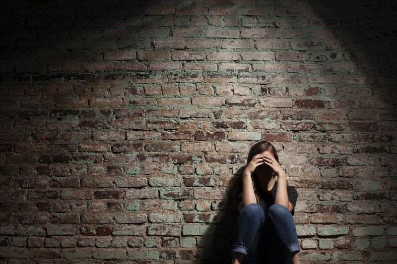 Sad woman sitting alone against brick wall.