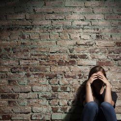 Sad woman sitting alone against brick wall.