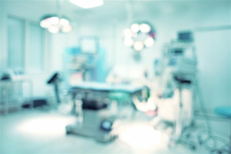 A blurred photo of an operating theatre showing an operating table and various other forms of equipment and lighting surrounding it. 