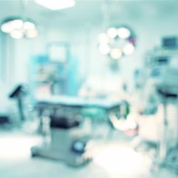 A blurred photo of an operating theatre showing an operating table and various other forms of equipment and lighting surrounding it. 