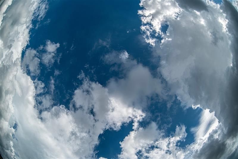 A photo with a fish-eye lens showing the view of an abject returning to Earth from space. The image is of blue sky and clouds surrounding it. 