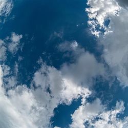 A photo with a fish-eye lens showing the view of an abject returning to Earth from space. The image is of blue sky and clouds surrounding it. 