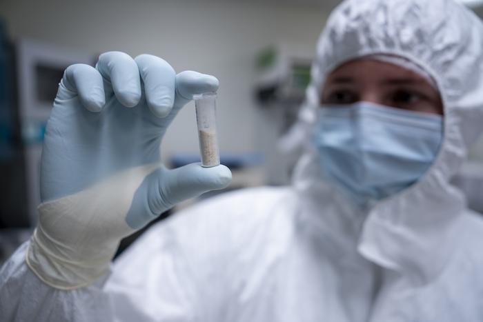 Scientist in protective gear holds up a test tube contain mammoth tusk power.