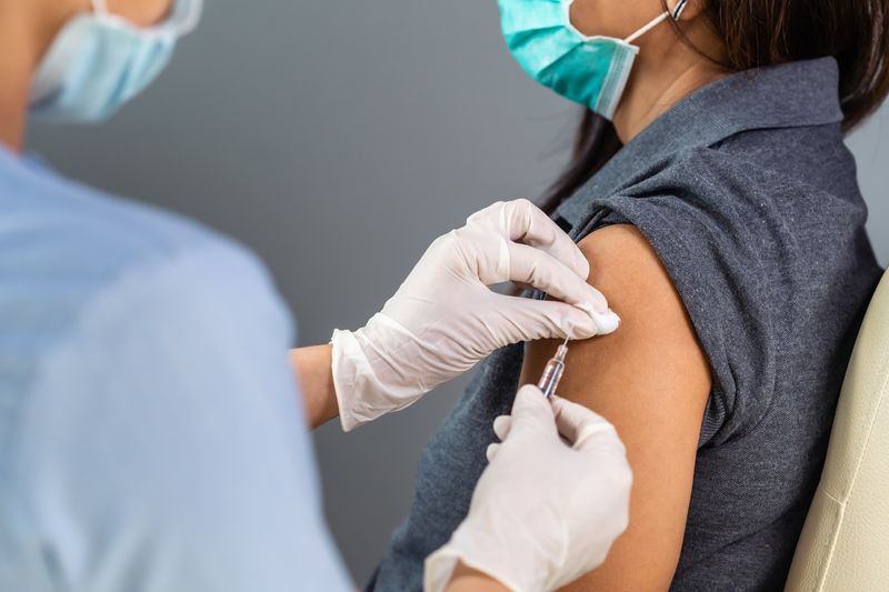 close up of a doctor holding a syringe and using a cotton ball before giving an injection to a patient in medical mask