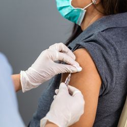 close up of a doctor holding a syringe and using a cotton ball before giving an injection to a patient in medical mask