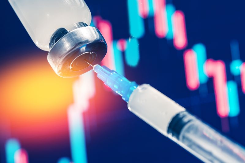 close up of vaccine being drawn into syringe from a vial with a red and blue graph lit up in the background