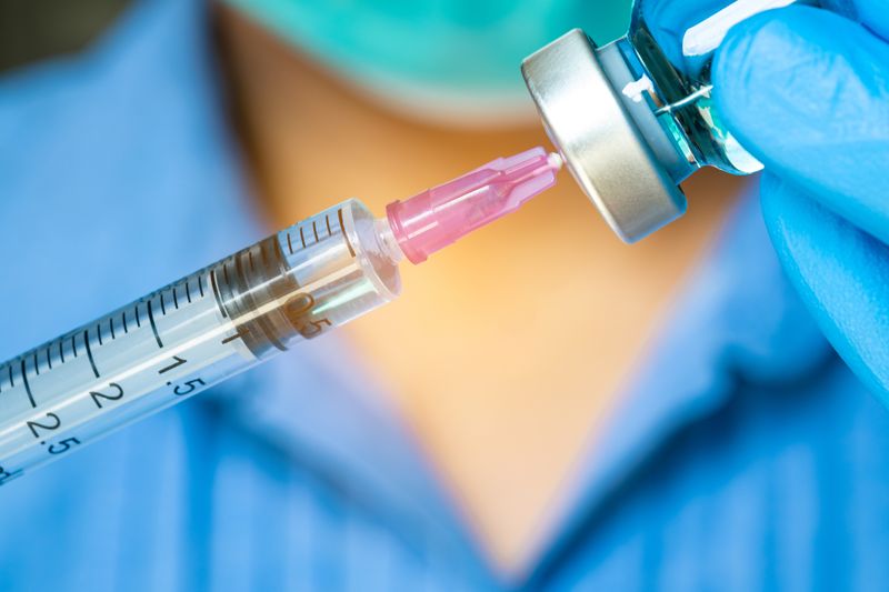 close-up of syringe inserted into vaccine vial