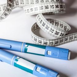 injection pens, used to administer drugs like Ozempic, on a table with a curled up tape measure