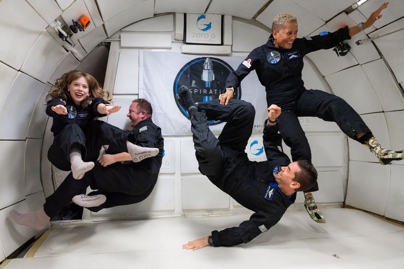 crew of Inspiration4 training in microgravity; 4 people in blue overalls floating around a white chamber