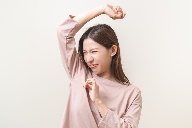 Woman in pink shirt sniffing her own armpit with a disgusted expression