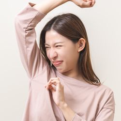 Woman in pink shirt sniffing her own armpit with a disgusted expression