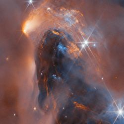 Whispy dark clouds are intersped with bright glowing ones, together with bright stars and smaller dot-like object in this panorama of a nebula.