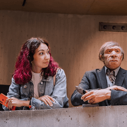 Homo sapiens (human) standing next to a model of a Neanderthal dressed like a modern human. 