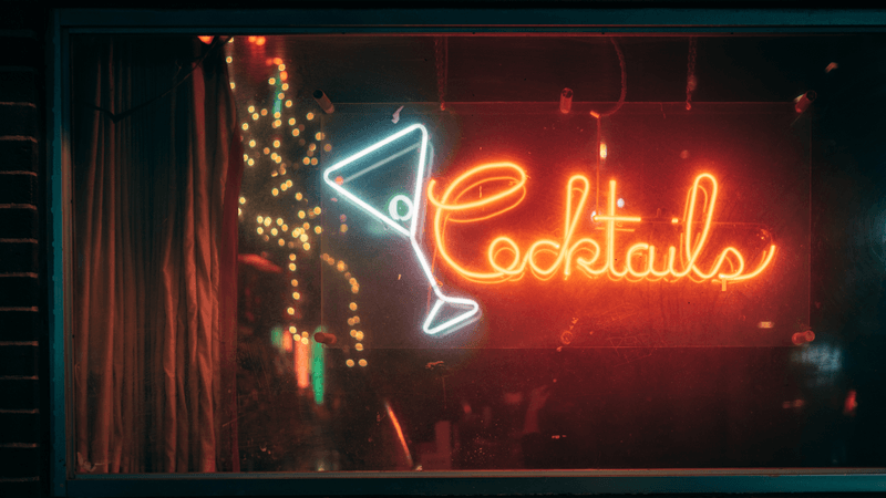 a neon light in a bar window spelling out "cocktails"