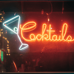 a neon light in a bar window spelling out "cocktails"