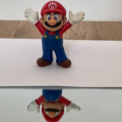 A Mario statuette sits on a piece of paper on a mirror, which should be hidden from the mirror by the paper. Given the angle, however, part of the statue is visible in the mirror.