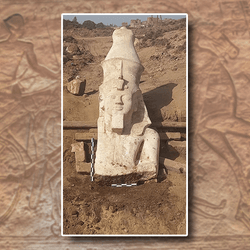 A photo of the upper portion of the newly discovered Ramesses II statue. The image depicts the pharaoh's head wearing a double crown, headdress and royal serpent. The statue portion stops around the middle of his chest and he is missing his right arm. The whole image has been superimposed on a photo of a hieroglyphic depiction of Ramesses II riding on a chariot at the battle of Kadesh in the Great Temple of Abu Simbel.